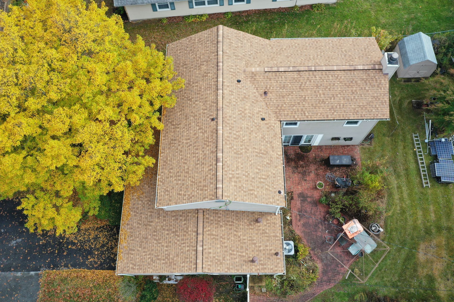 Aerial view of a tan-roof house with a large yellow tree and a small backyard patio.