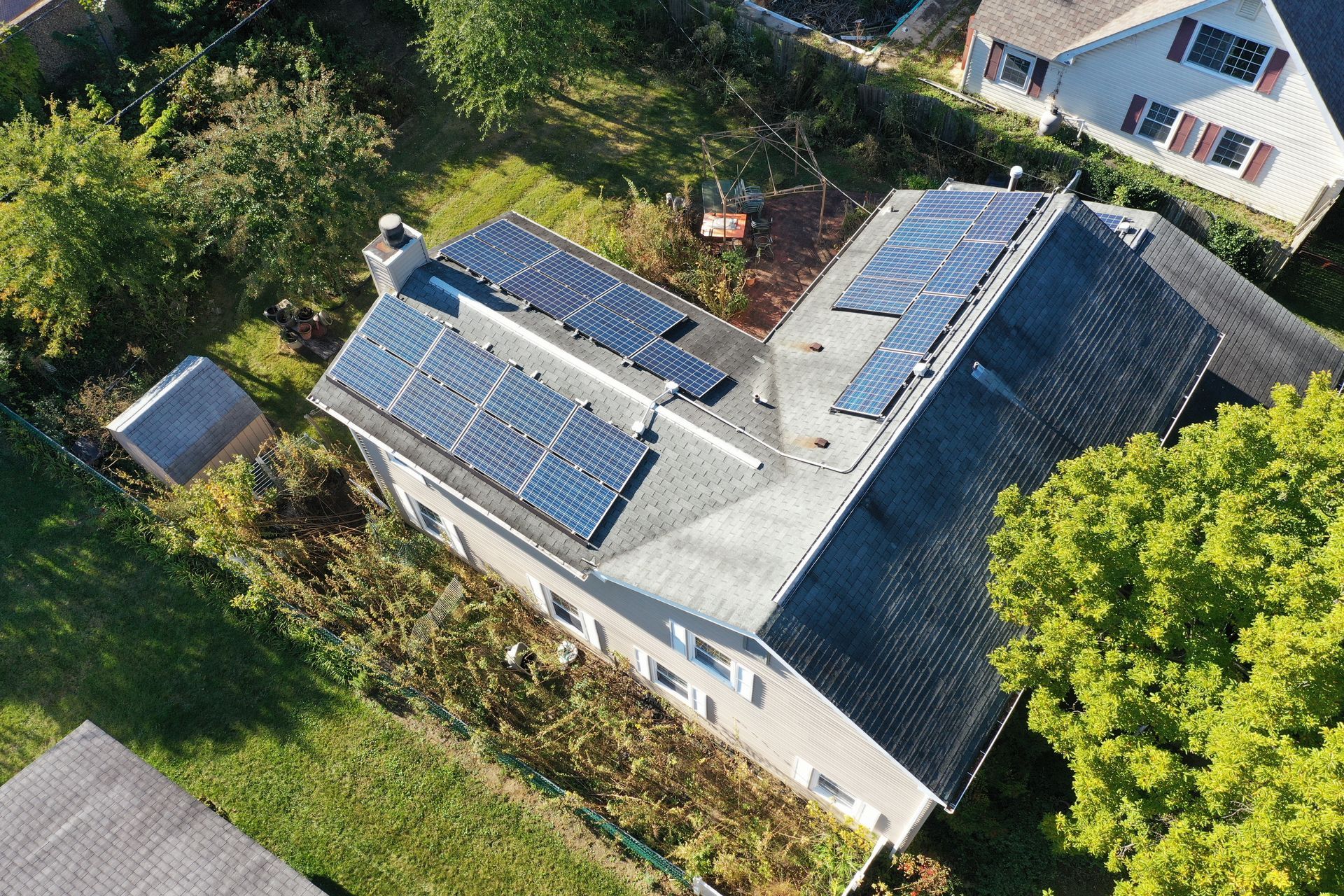 Aerial view of a house with multiple solar panels on the roof, surrounded by trees and greenery