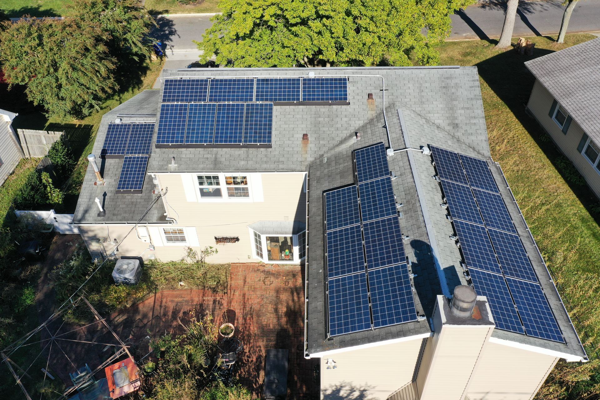 Aerial view of a house with blue solar panels on the roof, surrounded by trees and a yard.