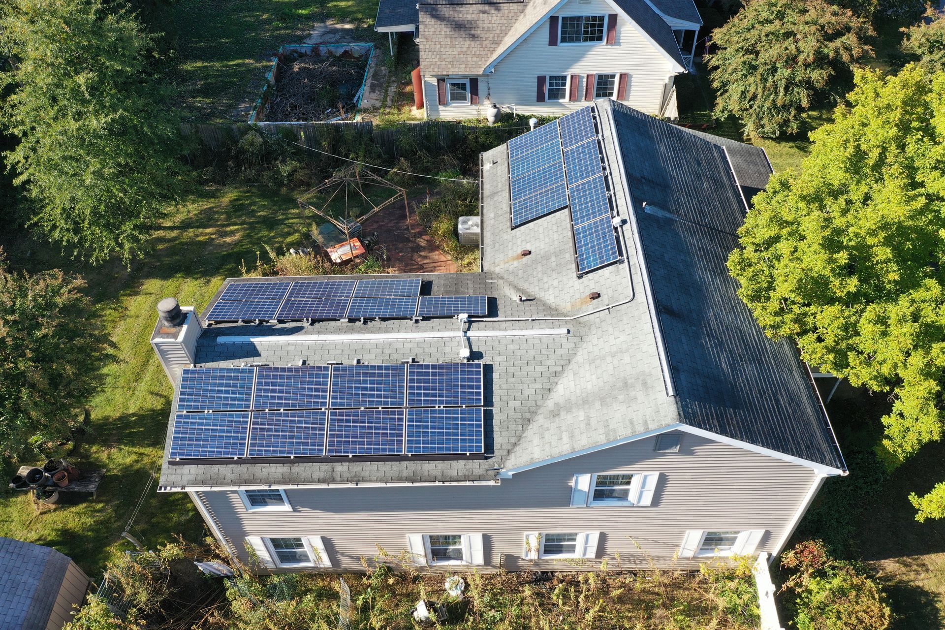 Aerial view of a house roof with several solar panels and surrounding trees
