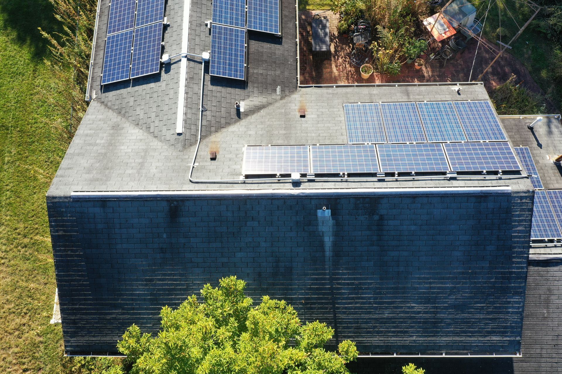 Aerial view of a house roof with solar panels and a tree in the foreground
