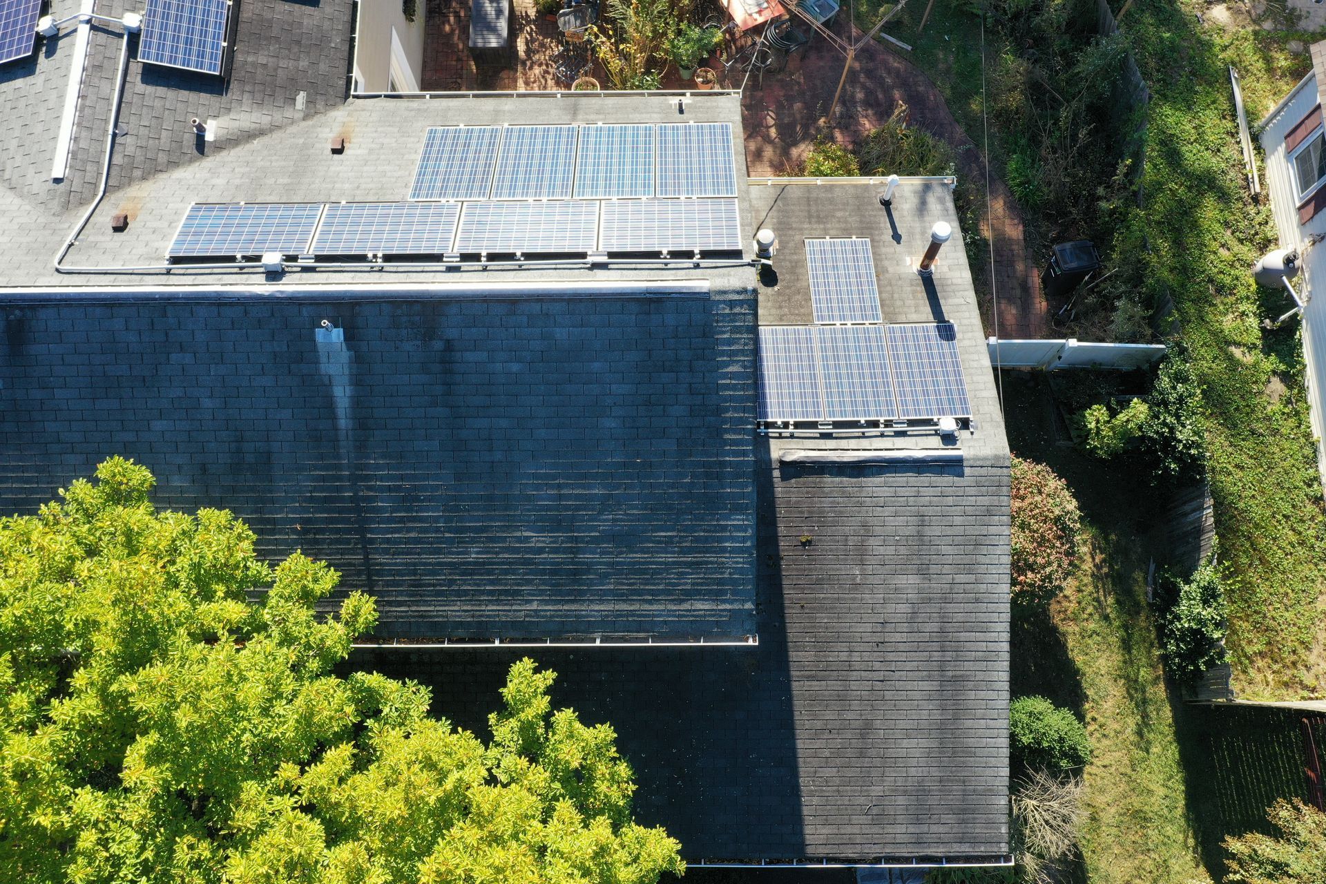 Aerial view of dark rooftops with solar panels, trees, and a narrow driveway between houses