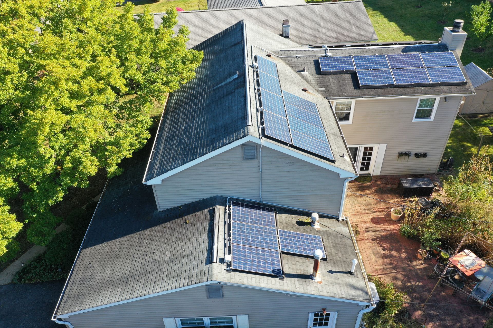 Aerial view of two rooftops with solar panels beside green trees and a driveway