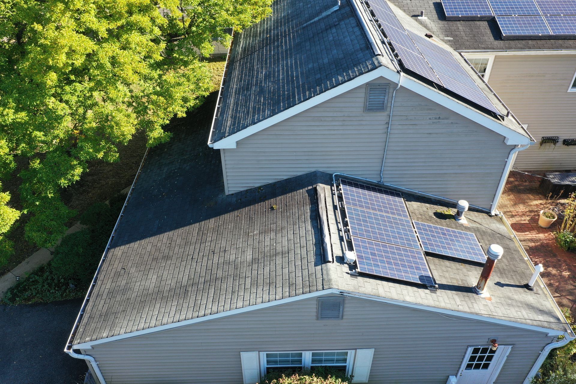 Aerial view of a house roof with solar panels and skylights, surrounded by trees.