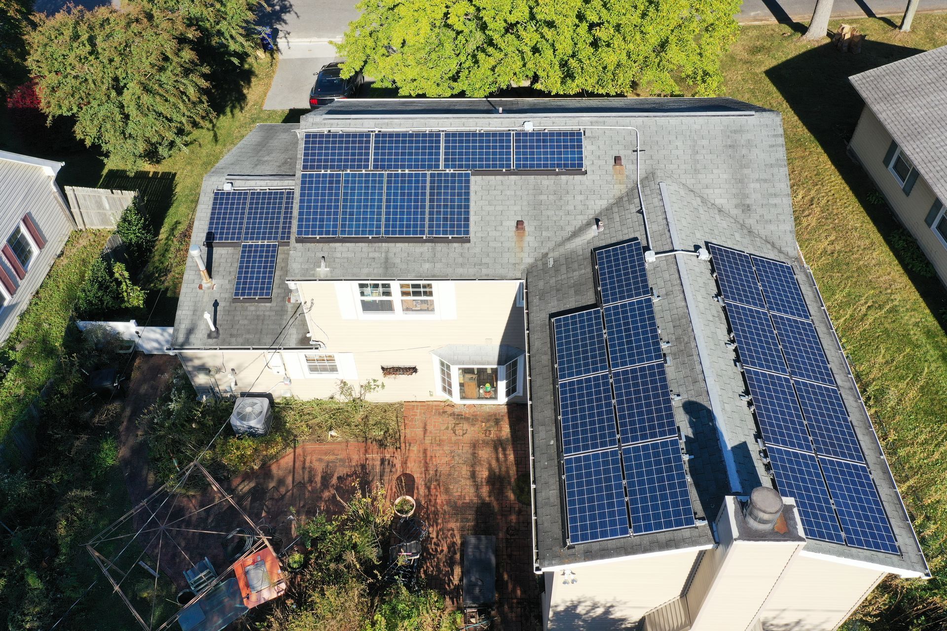 Aerial view of a house with blue solar panels on multiple roof sections and a backyard.