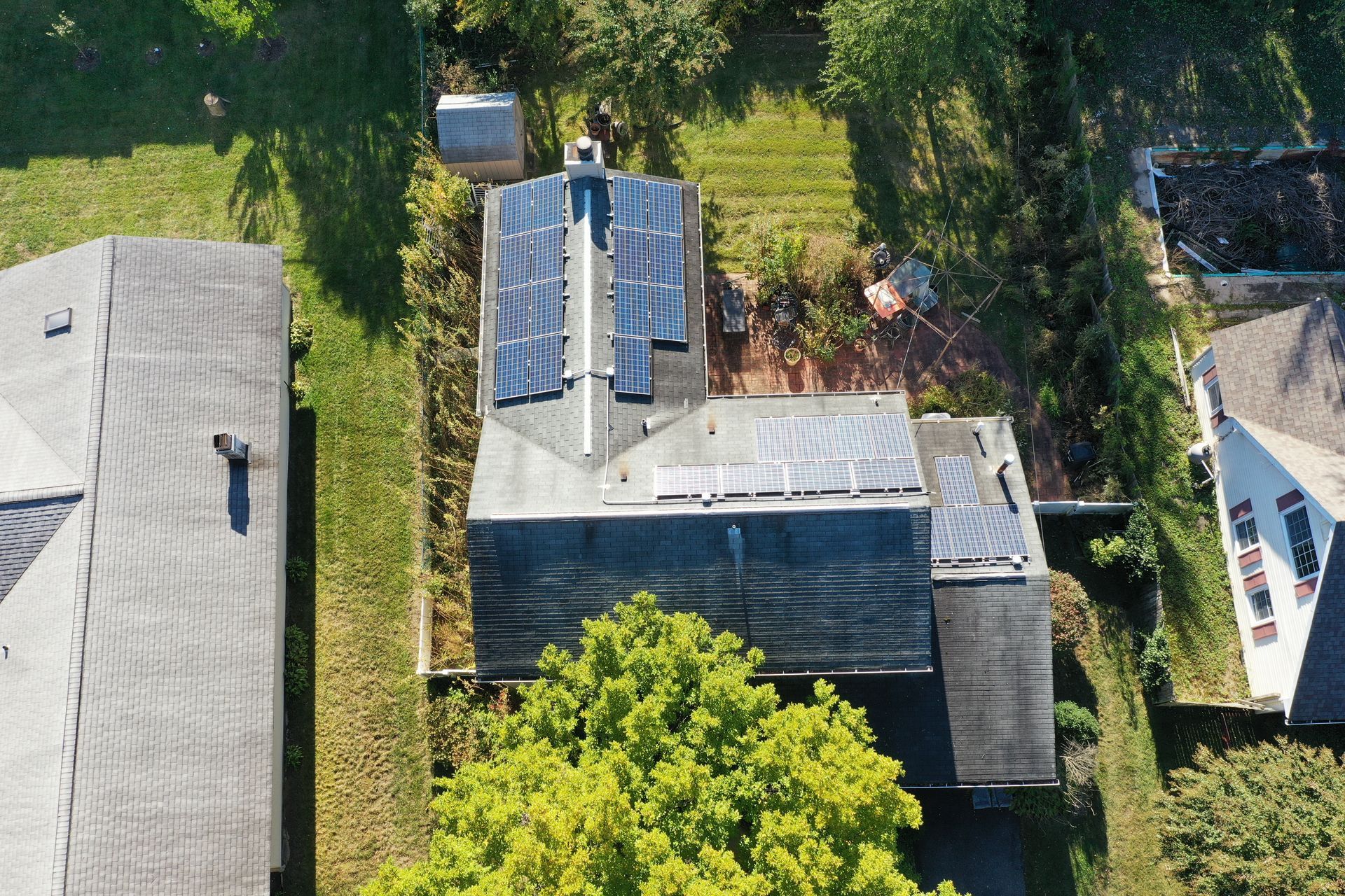 Aerial view of several houses with gray roofs, trees, and a central rooftop with solar panels.