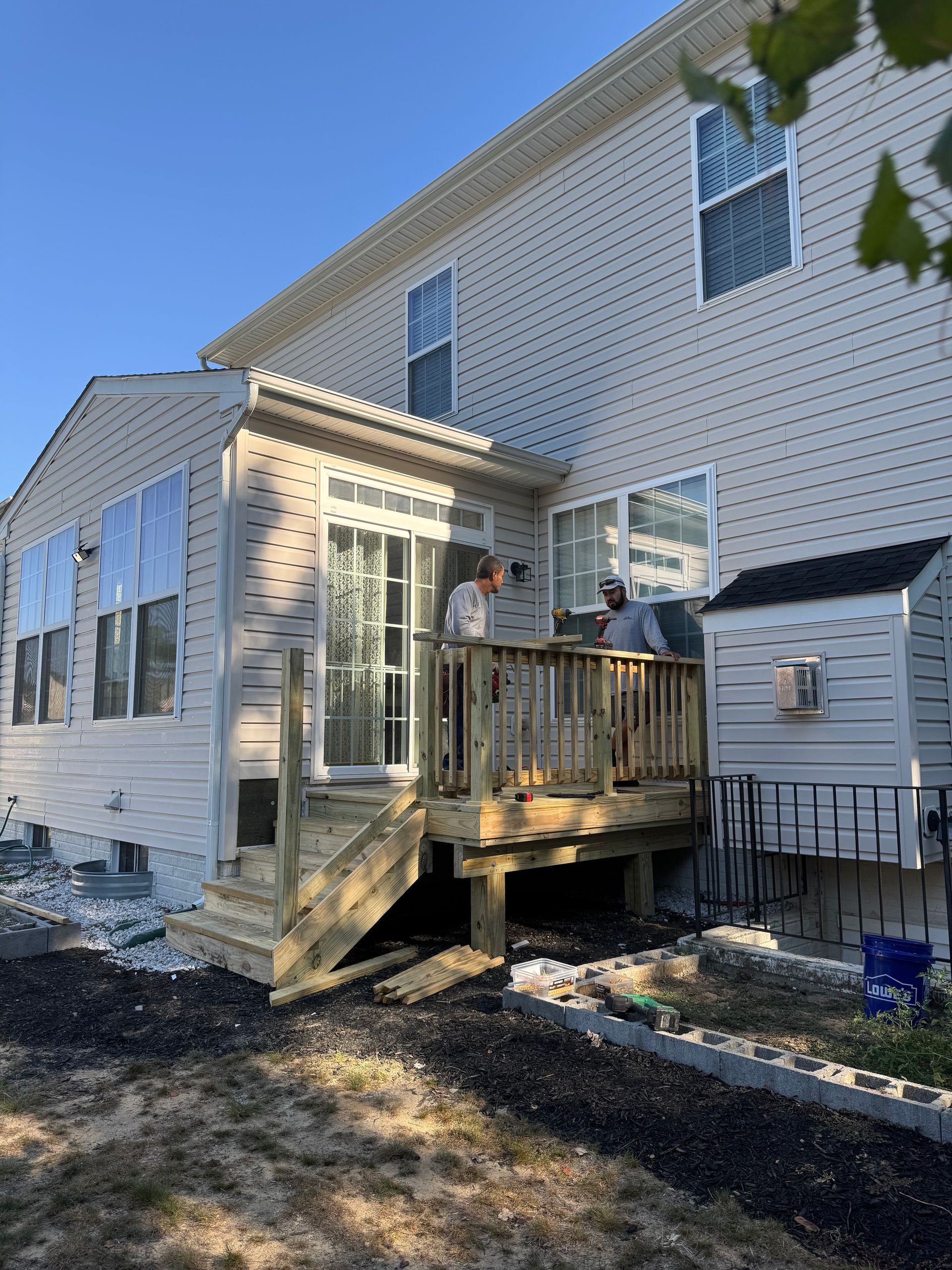 White two-story house with a small wooden deck, stairs, and sliding glass doors in a sunny yard