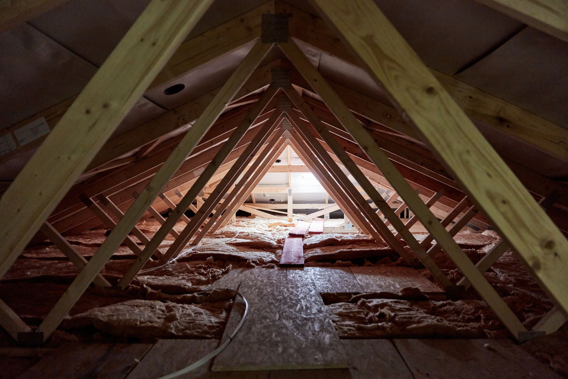 Attic interior with wooden trusses and insulation, viewed down a narrow central walkway