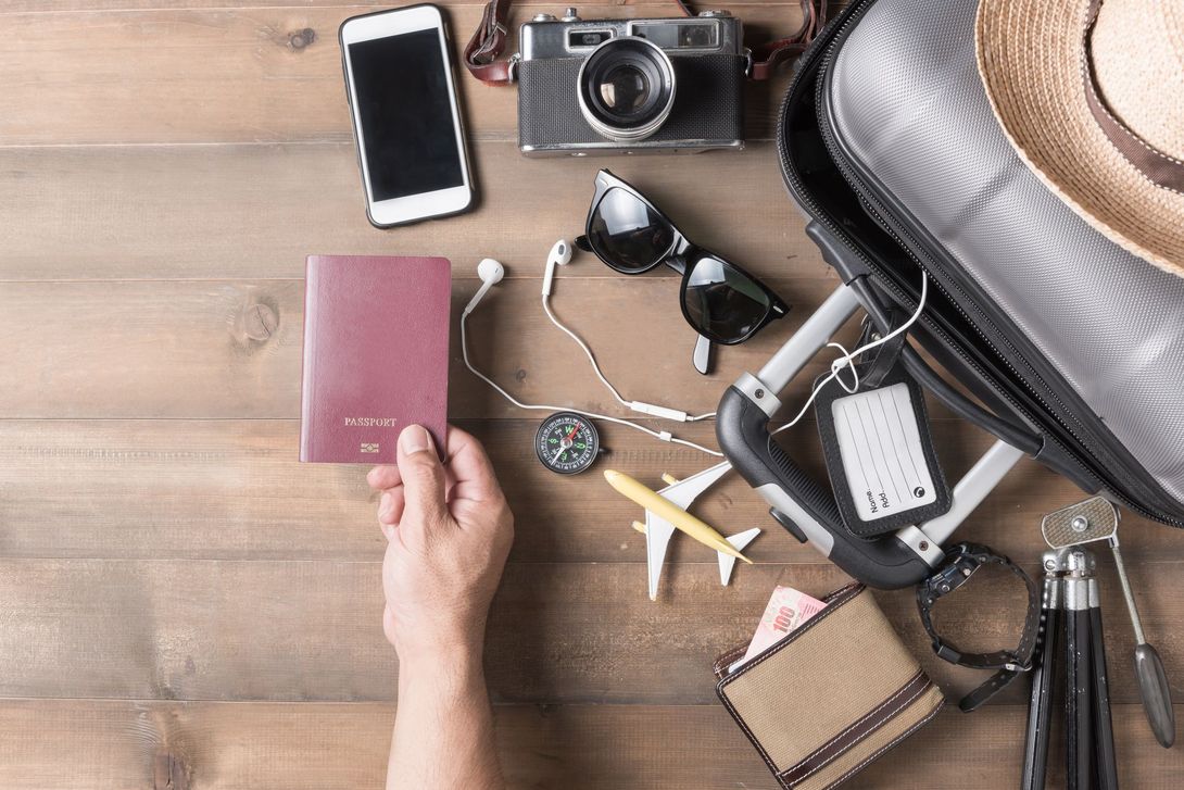 Travel essentials arranged on a wooden table with a hand holding a burgundy passport