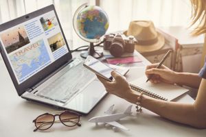 Person studying at a desk with laptop, globe, notebook, and glasses in warm sunlight