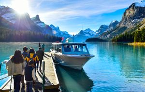 People boarding a boat docked at a turquoise mountain lake under a bright blue sky