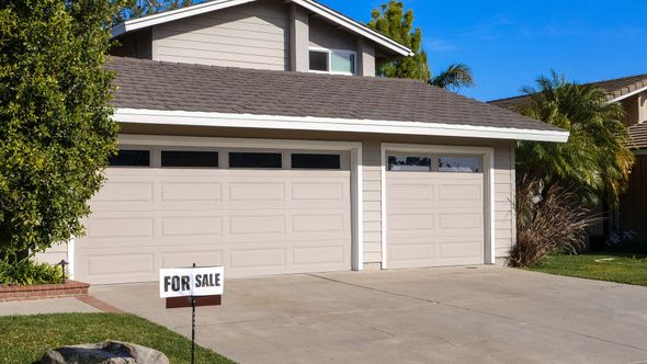 Suburban house with a three-car garage and a FOR SALE sign in the driveway