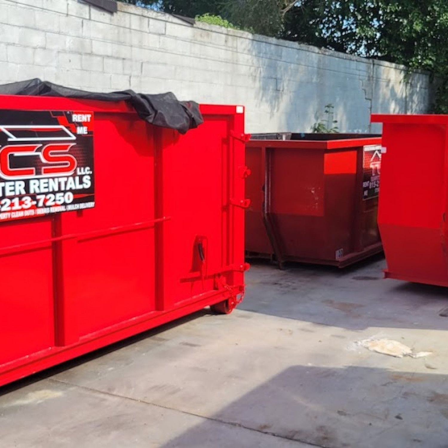 Three red dumpsters lined up against a wall; dumpster rental company logo visible.