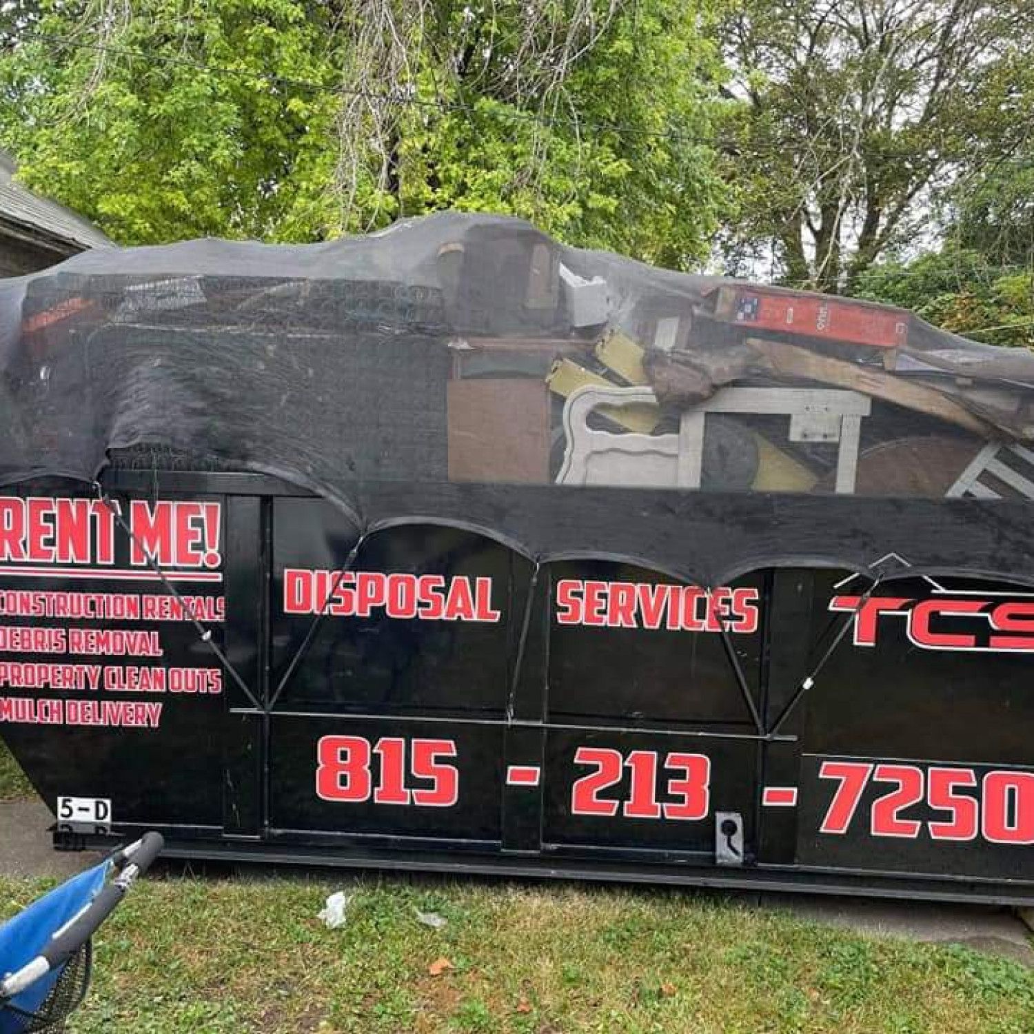 Black dumpster filled with debris and covered with netting;
