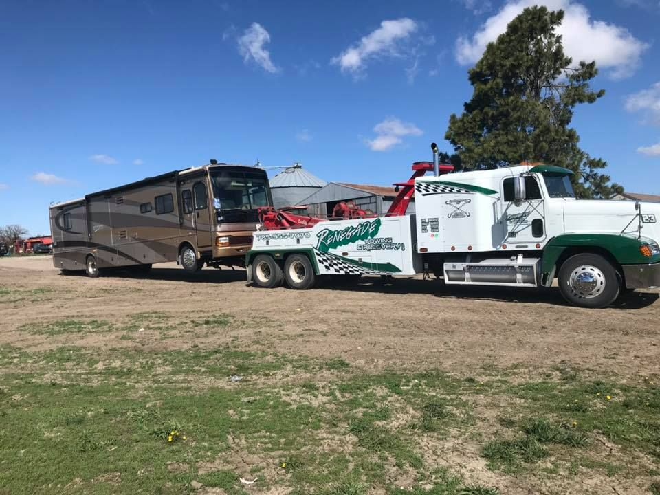 A tow truck is towing a rv in a field.