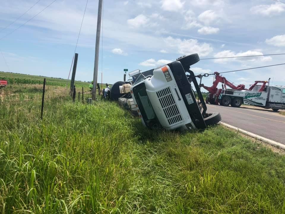 A truck is laying on its side on the side of the road.