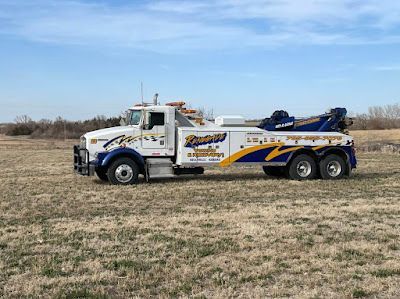 A white and blue tow truck is parked in a grassy field.