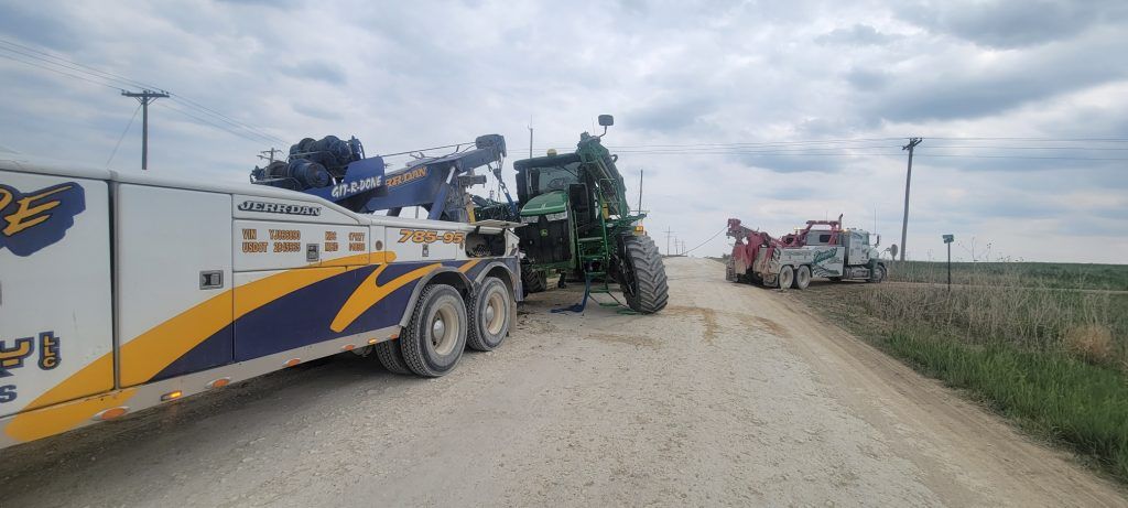 A tow truck is towing a tractor down a dirt road.