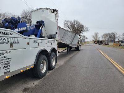 A tow truck is towing a semi truck down a road.