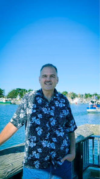 A man with a mustache is wearing a brown shirt and smiling.