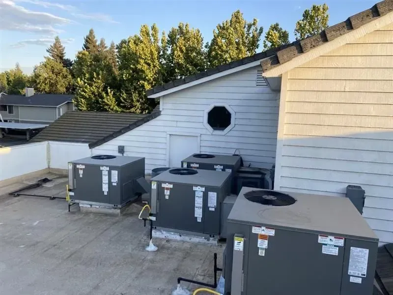Rooftop HVAC units beside a white building with trees in the background