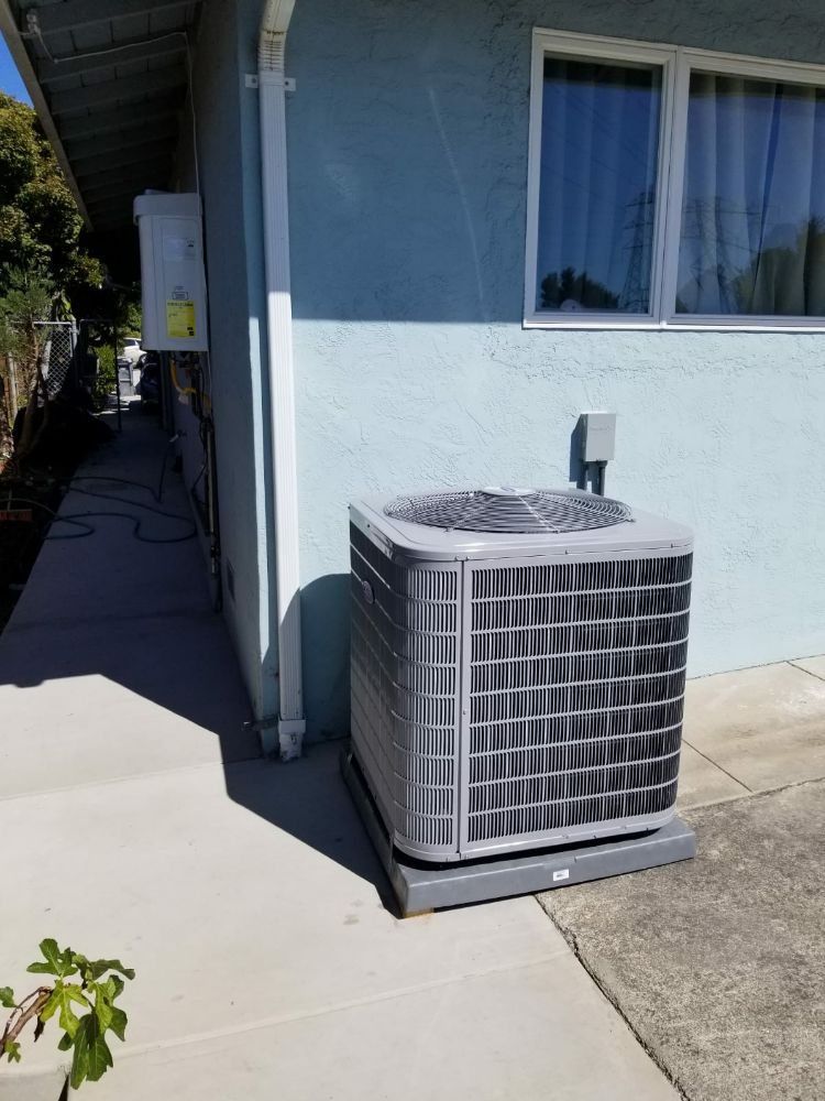 Outdoor air conditioner unit beside a blue house wall and window on a concrete patio