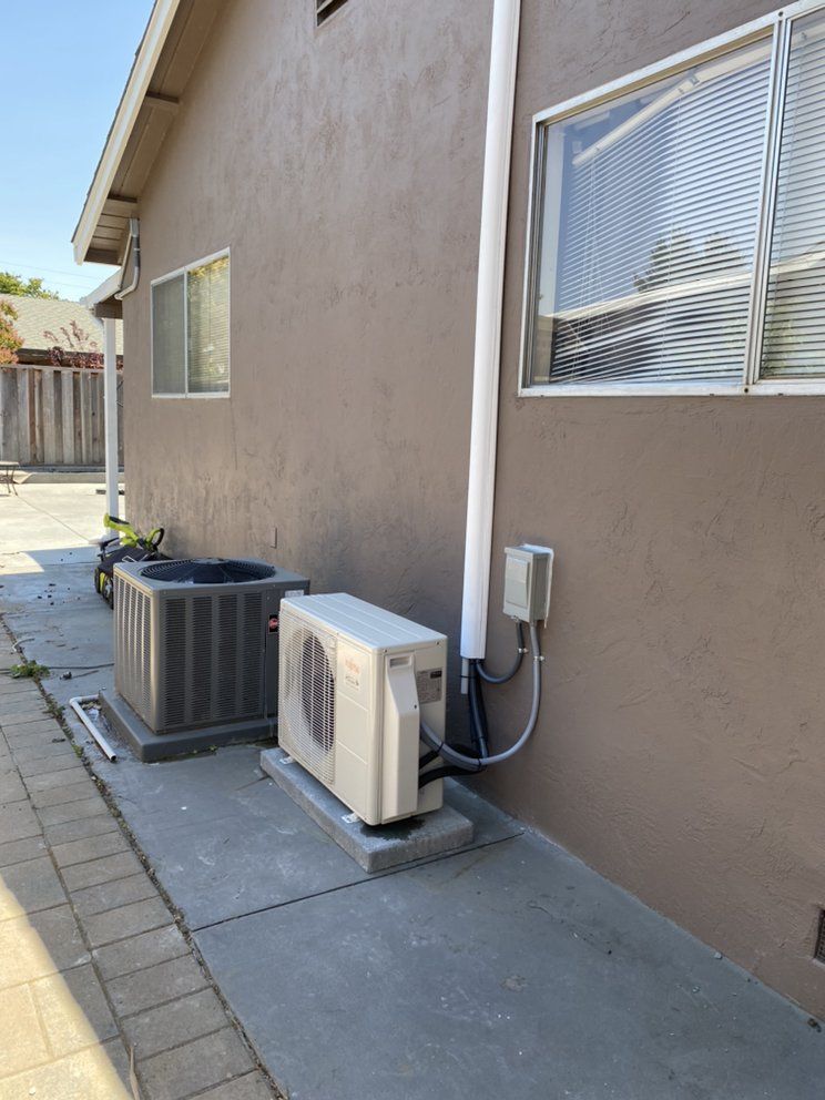 Side yard exterior with two HVAC units beside a beige stucco house and window