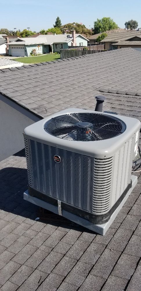 Roof-mounted air conditioner unit on a gray shingled roof under a clear sky