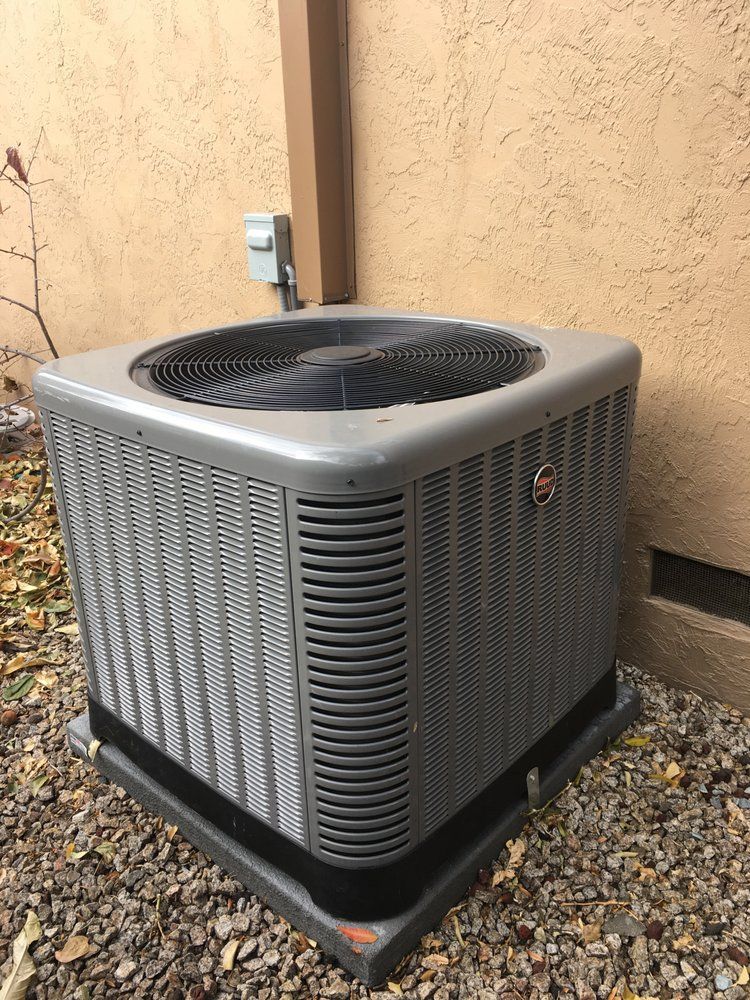 Outdoor air conditioner unit beside a beige stucco wall and utility pipe