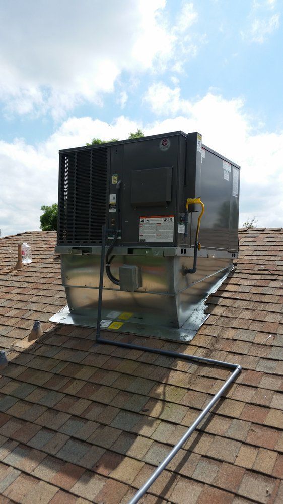 Large black HVAC unit on a shingled roof under a partly cloudy sky.