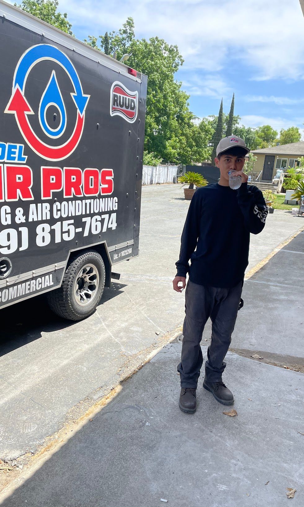 Person in black clothing and cap standing beside a truck with a large HVAC and air conditioning logo.