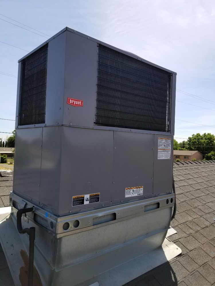Large gray rooftop HVAC unit with black vents on a building roof under a clear sky