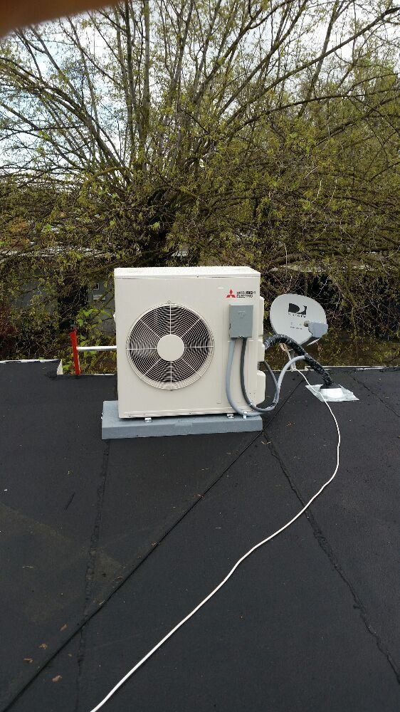 Outdoor HVAC unit and white satellite dish mounted on a flat black rooftop, with trees in the background
