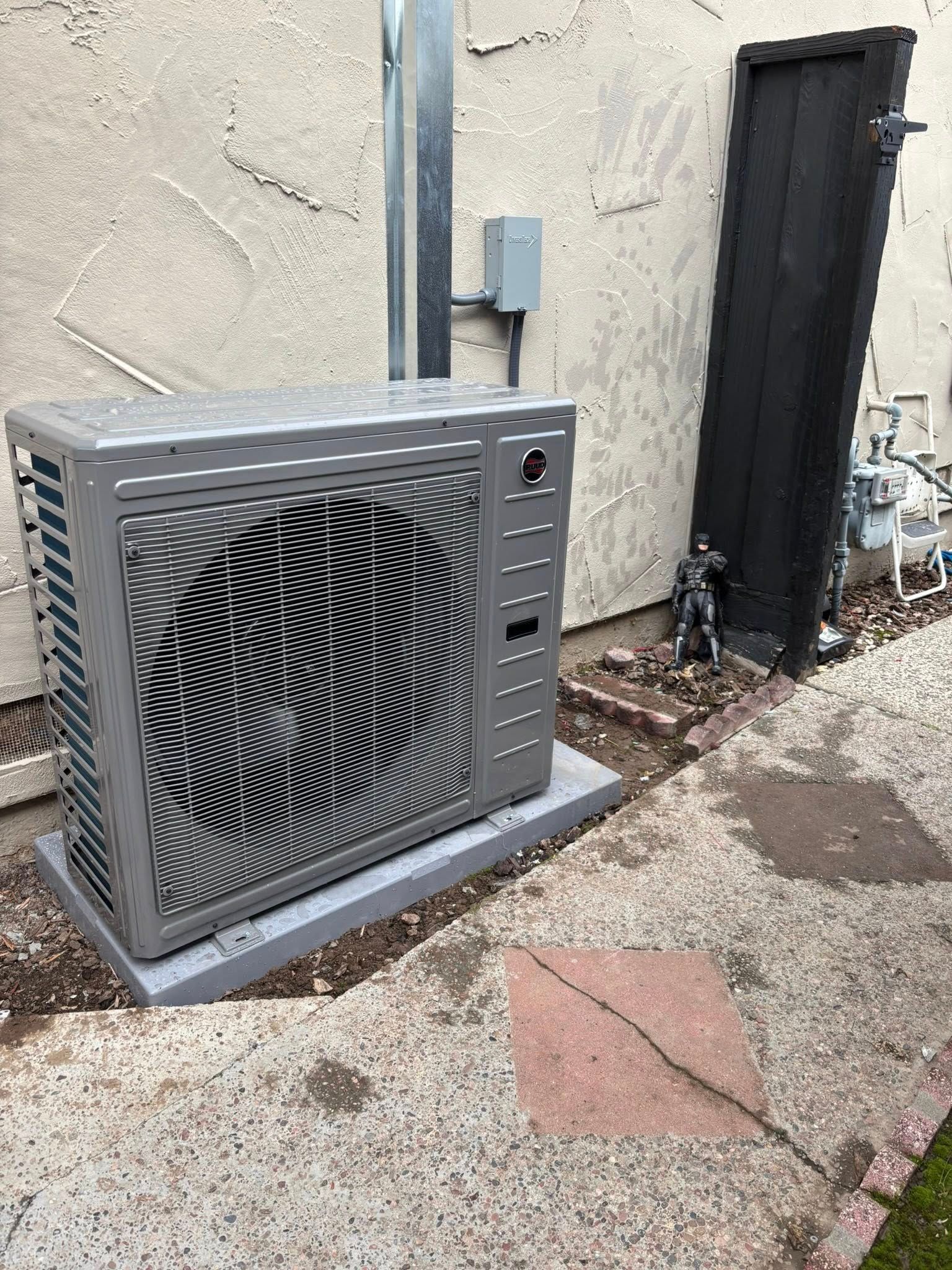 Outdoor HVAC unit beside a stucco wall and dark door on a gravel patio