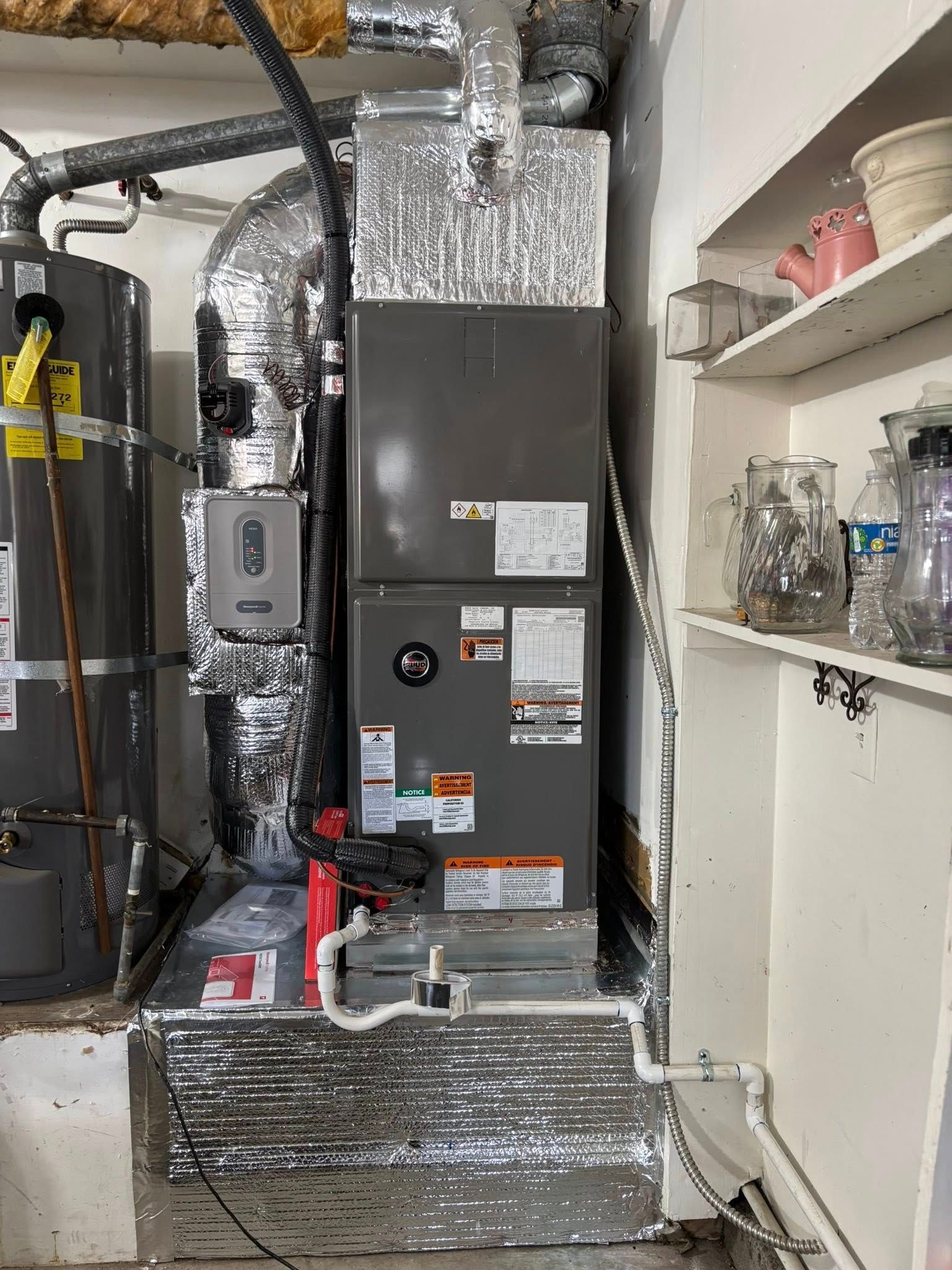 Central HVAC furnace with silver ductwork and insulated pipes in a utility closet, shelves at right