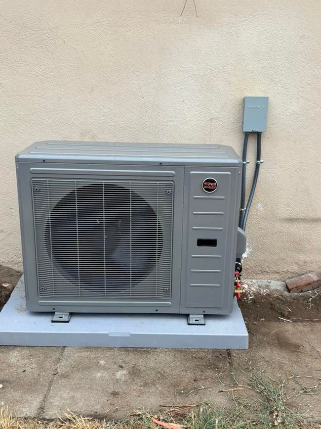 Outdoor air conditioner unit beside a wall, with a fan visible behind the grille.