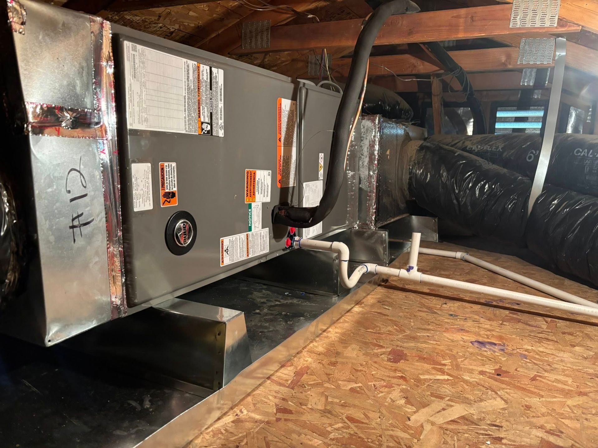 Attic HVAC unit with metal ductwork and insulated vents beside plywood flooring