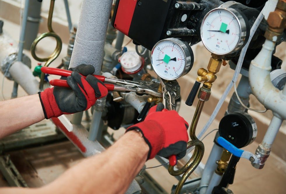 Technician’s gloved hands adjusting gauges and valves on industrial piping