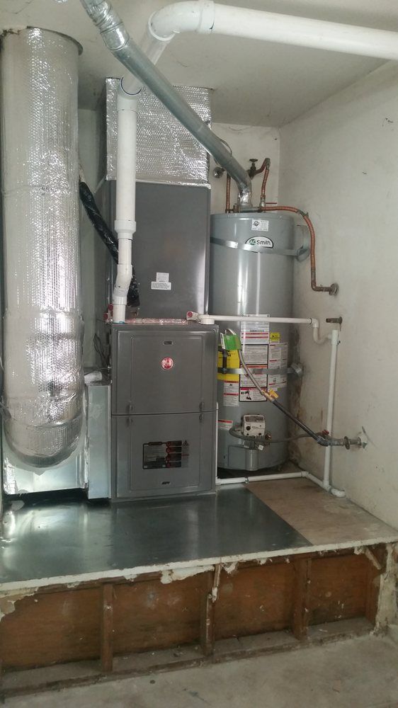 Basement utility room with furnace, water heater, and insulated ductwork on a raised platform.