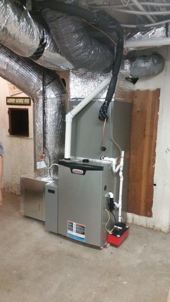 HVAC furnace unit in a utility room with exposed ducts and a broom leaning against it
