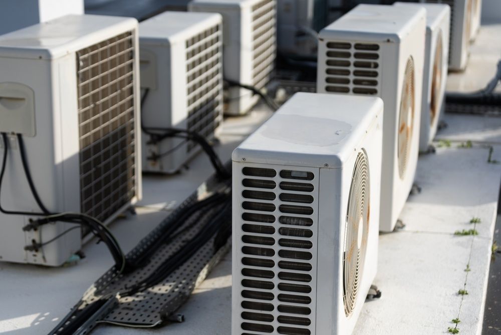Outdoor row of white air-conditioning units with black cables on a rooftop or terrace.