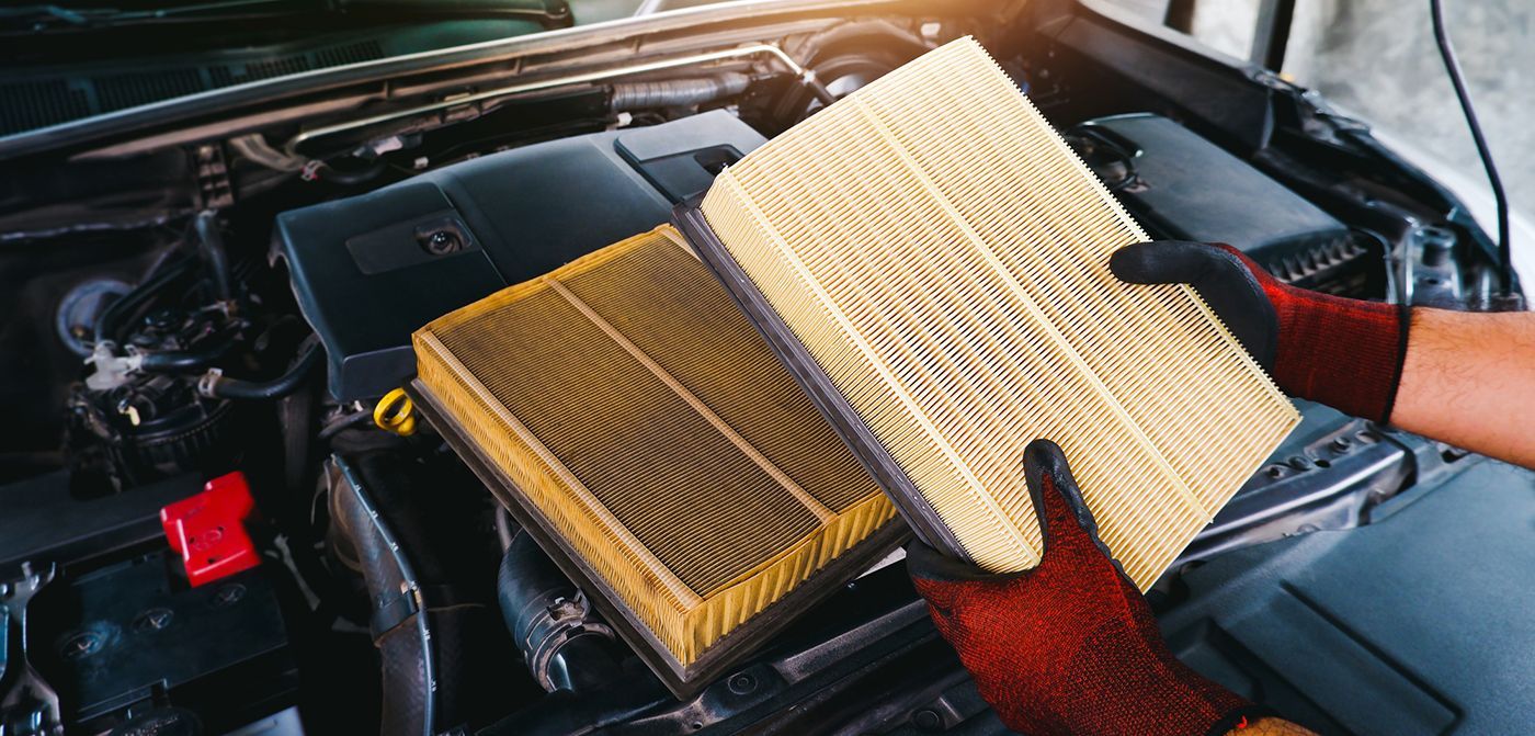 A person is holding two air filters in front of a car engine.