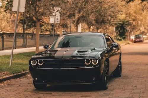 Black Dodge Challenger with racing stripes parked on a brick road.