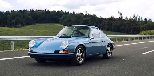 Blue Porsche 911 on a highway with a forest background.