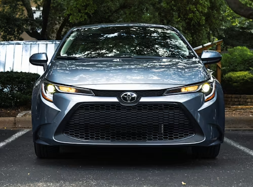 Front view of a gray Toyota sedan parked on a driveway, with headlights on.