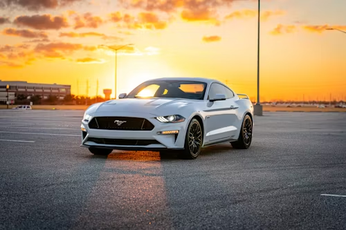White Ford Mustang parked on asphalt at sunset.