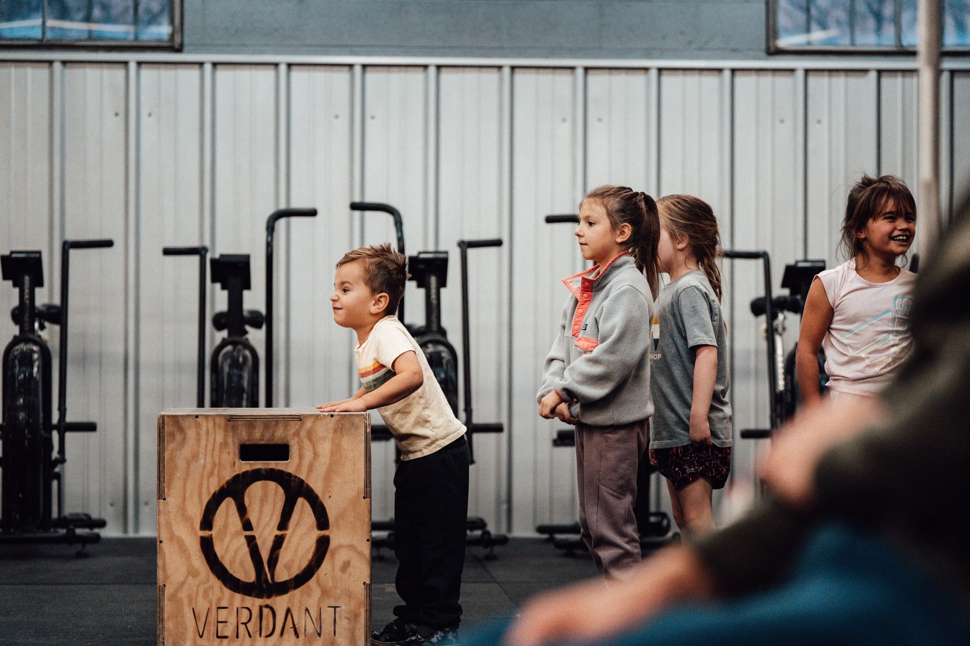 Children in a Boise-area gym, one child on a wooden box, others watching; gym equipment in background.