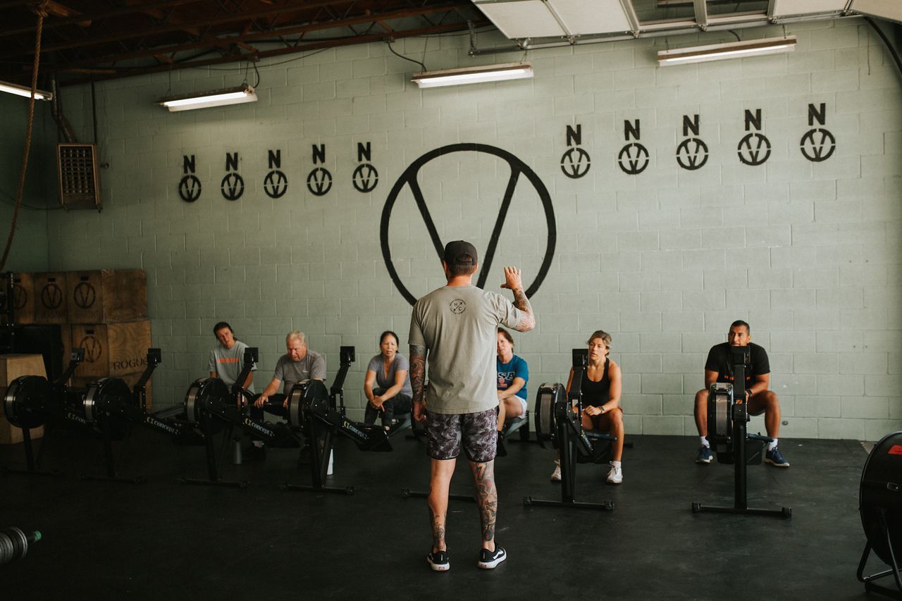 Instructor leading a workout class at a CrossFit gym in Star, ID with rowing machines; people listening.