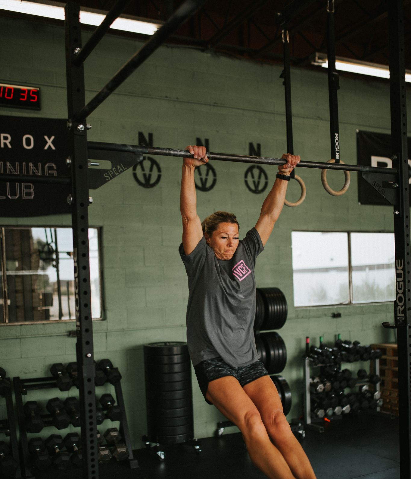 Woman doing pull-ups on a bar at a gym in Star, ID. She is wearing a gray shirt and shorts.