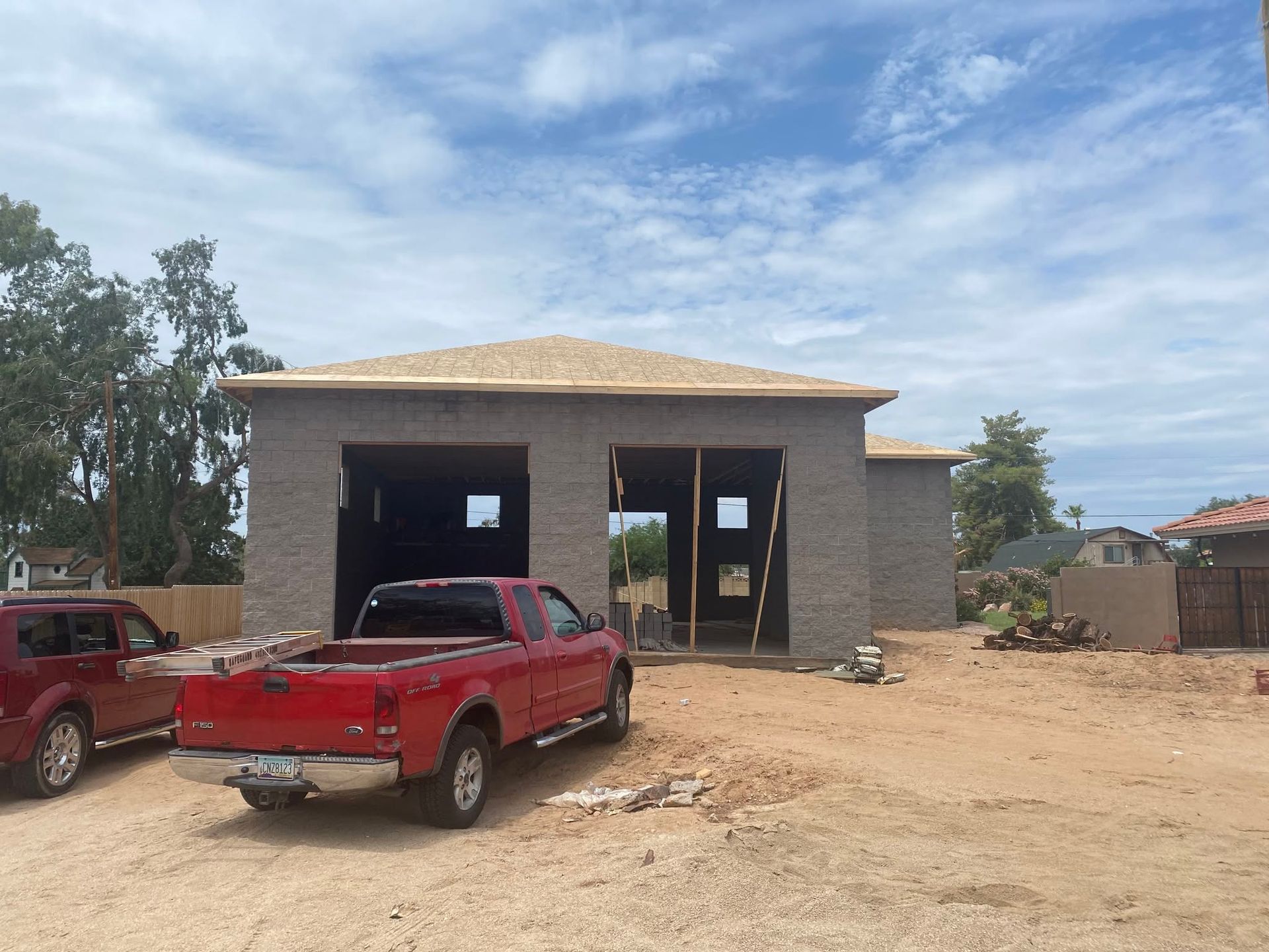 Two red pickup trucks parked outside a partly finished brick building under a blue sky